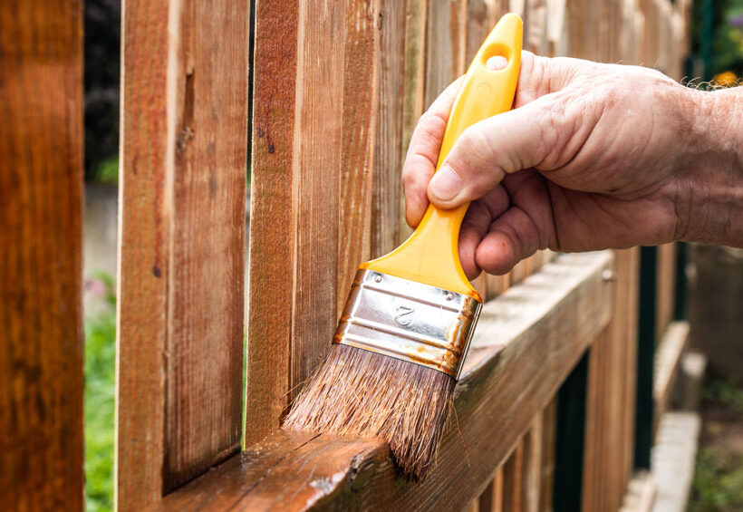 man-applying-stain-to-wooden-fence
