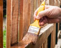 man-applying-stain-to-wooden-fence