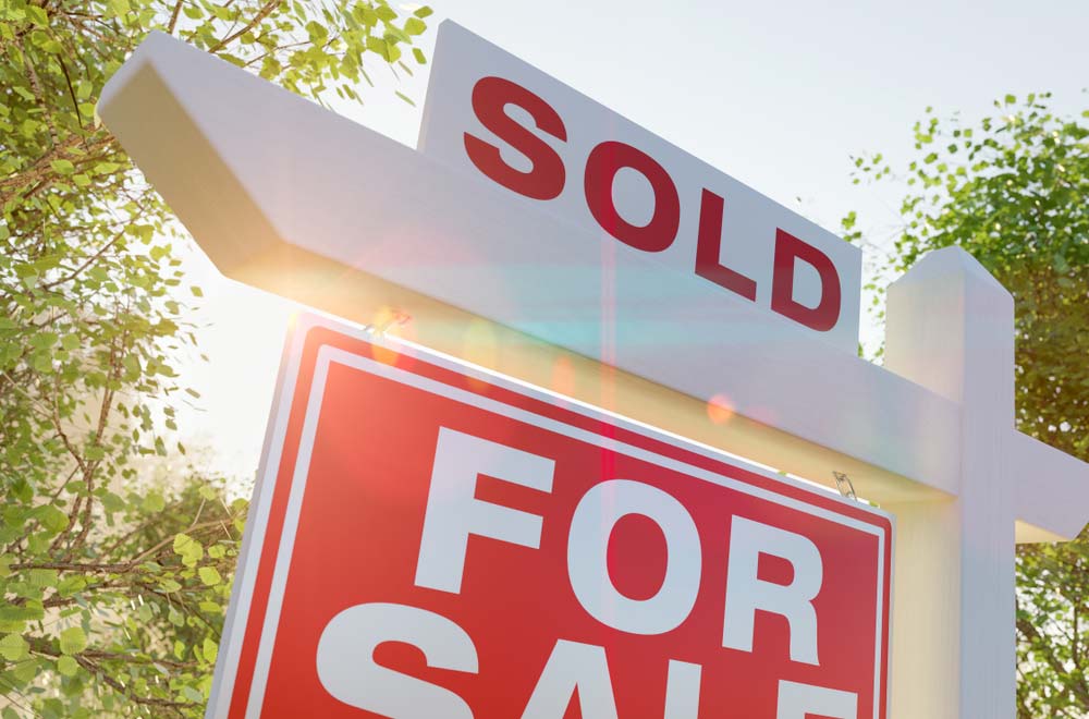 A “Sold” sign sits above a “For Sale” sign in a yard.