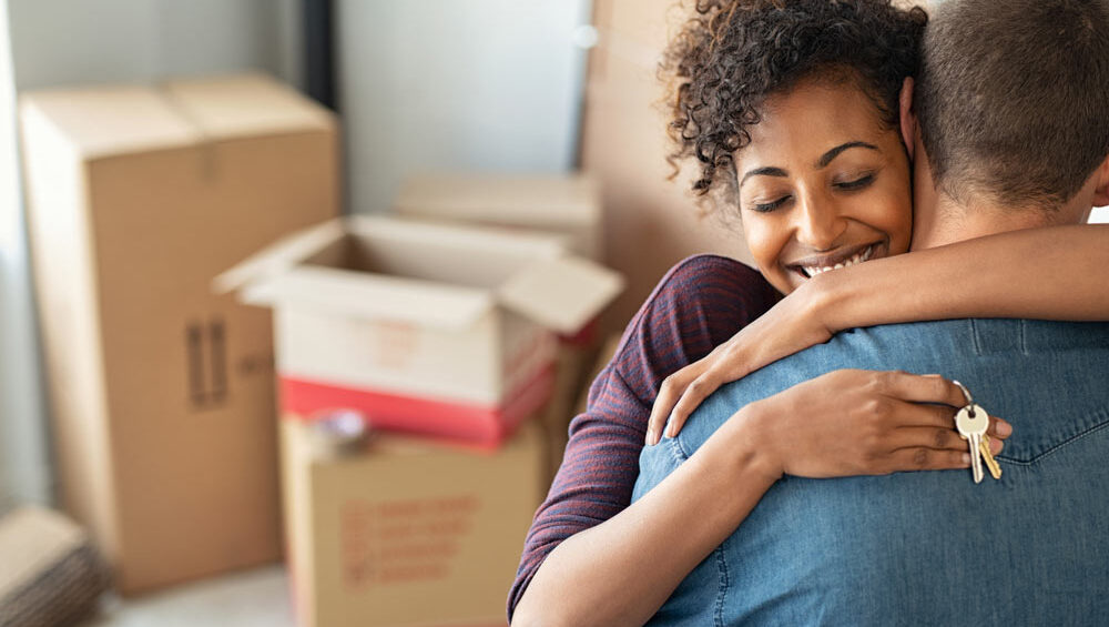 A woman hugs her husband, holding keys to their new home in her hand.