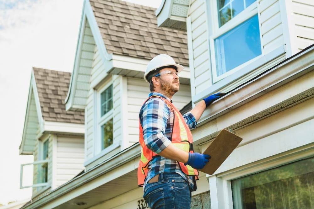 A home inspector checks out the gutters and roof of a home.